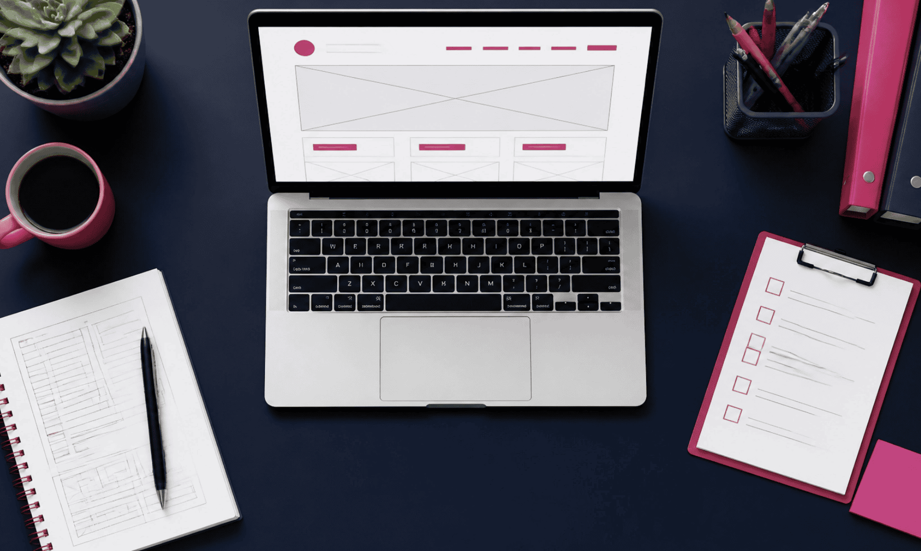 A laptop displaying a website on a dark desk with notebooks, a cup, and stationery.